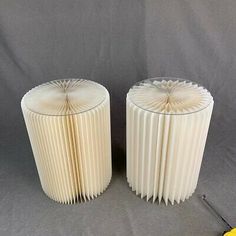 two white vases sitting next to each other on a gray surface with a yellow object in the foreground