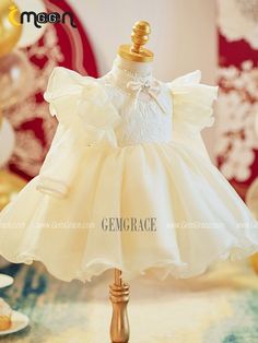 a white dress on a mannequin stand in front of some gold foil balloons