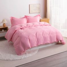 a bed with pink comforter and pillows in a room next to a white rug