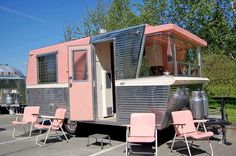 a pink and silver trailer parked in a parking lot next to two lawn chairs on the ground