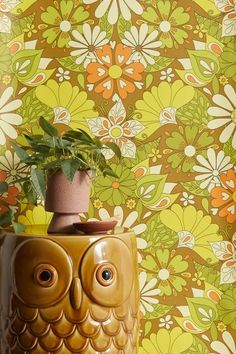 an owl planter with a potted plant on it in front of a floral wallpaper