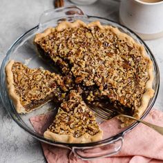 a pie on a glass plate with a fork and cup of coffee in the background