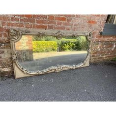 an old mirror sitting on the ground next to a brick wall