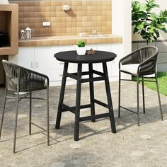 three chairs and a table outside on the patio with an outdoor kitchen in the background