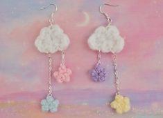 three small crocheted flowers are hanging from silver hooks on a pink and purple background