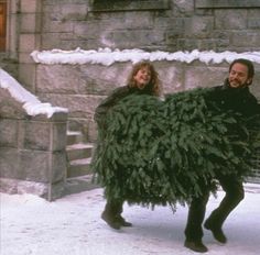 a man and woman carrying a christmas tree in the snow