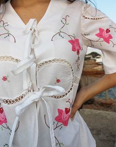 Tie front blouse in white with hand embroidered floral details and crochet panels. V neckline. Short sleeve. Ties to front. Size M, EU 38-42 / UK 10-14. Measurements: 40"/ 102cm bust - 12" / 30cm sleeve length - 25" / 64cm blouse length. Condition - New. Material - Cotton. Sustainability - Remade by our in house team using vintage fabrics. Model is a UK 6/8 & 5'7" tall. Spring V-neck Blouse With Lace Work, Fitted V-neck Embroidered Top For Spring, White Feminine Embroidered Short Sleeve Top, Feminine White Embroidered Top, Summer V-neck Top With Lace Work, Feminine Fitted Embroidered Top For Summer, Bohemian Broderie Anglaise Short Sleeve Blouse, White Short Sleeve Top With Lace Work, White Cotton Feminine Peasant Top