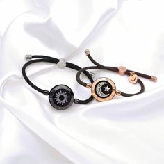 two bracelets with black and rose gold charms on white silk background, closeup