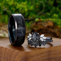 two wedding bands with black diamonds on them sitting on top of a wooden table next to each other