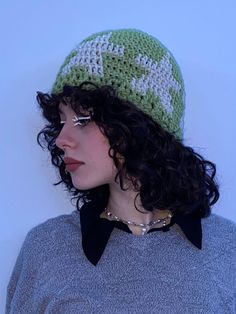 a woman wearing a green and white crochet hat with black collar, standing in front of a white wall