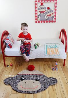 a young boy sitting on top of a bed next to a monkey rug and stuffed animal