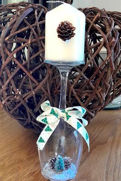 a candle is sitting in a wine glass with a pine cone on the top and ribbon around it