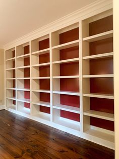 an empty room with red and white bookcases on the wall, hardwood flooring