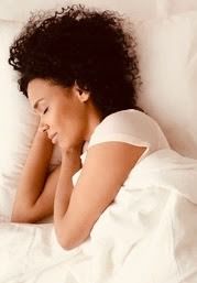 a woman laying in bed with her head on the pillow and looking at her cell phone