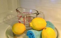 three lemons are sitting on a glass plate next to a measuring cup and towel