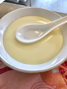 a white bowl filled with soup on top of a red checkered table cloth next to a spoon