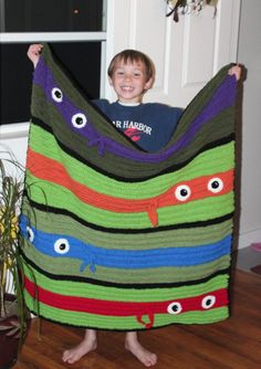 a young boy holding up a crocheted monster blanket