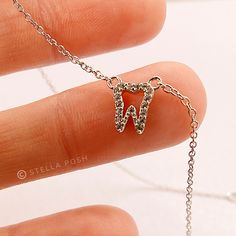 a hand holding a silver necklace with the letter n on it