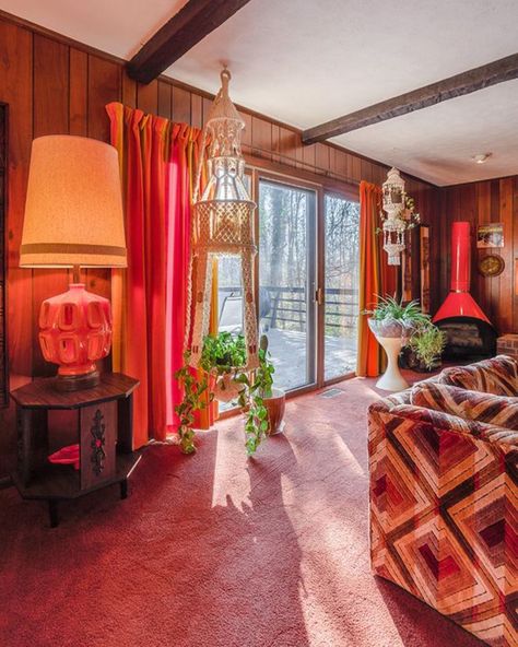 There is pink carpeting and dark wood paneling along all the walls. There is patterned couch partly in the frame on the right side, and in the back corner there is a red hearth. There are large sliding doors on the back wall that looks out to the back deck. There are two plant holders on either side of the sliding doors that are made of macrame. There is also a dark brown end table with a large red lamp on top. 70s Time Capsule Home, 1970 Apartment, 1970s Sunroom, 1970s Home Aesthetic, 70s Basement Aesthetic, 1970 Decor, 70’s Living Room, 70s Basement, 70s Living Room Aesthetic