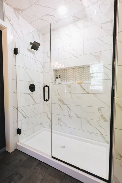 A beautiful modern farmhouse bathroom! Love the white marble tiled shower and the chevron tile in the niche. Mixed with the black accessories and faucets, it's stunning! A beautiful grey paint colour with blue vanity and a large barn door add to the farmhouse style. Beautiful choices for mirrors, wall lights, and tiles. A gorgeous remodel! Lockson Mix Marble Bathroom, Hall Bathroom Shower Ideas, Prefabricated Shower Stall, Bathroom Shower White Tile, All White Shower Tile, Affordable Shower Remodel, Porcelain Shower Wall Tile, Pan Shower Ideas, Large Shower Tile Ideas Small Bathrooms