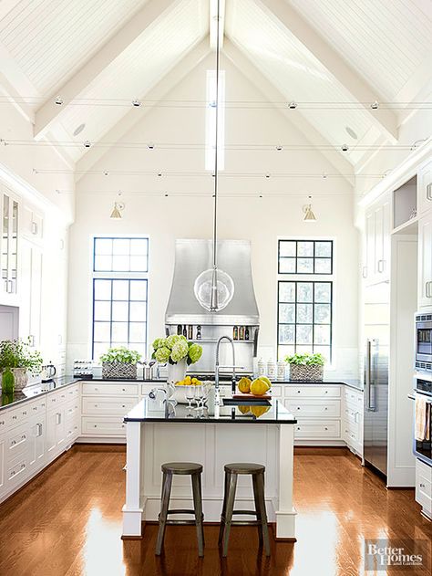 With the look of an old rural church, this kitchen is striking in its simplicity. Clad in beaded board and rafter-like beams, a cathedral ceiling reaches upwards and fashions a two-story wall at the range. The wall accommodates two sets of windows and a rectangular pane that pull abundant light into the large room. Cable lights that span the room's center and clear-glass pendants suspended from the ceiling's peak boast progressive profiles that give the classic kitchen a modern lift. Kitchens Without Upper Cabinets, Architecture Renovation, Modern Farmhouse Kitchen Decor, Farmhouse Kitchen Design, Bright Kitchens, Kitchen Trends, Modern Farmhouse Kitchens, Kitchen On A Budget, Large Kitchen