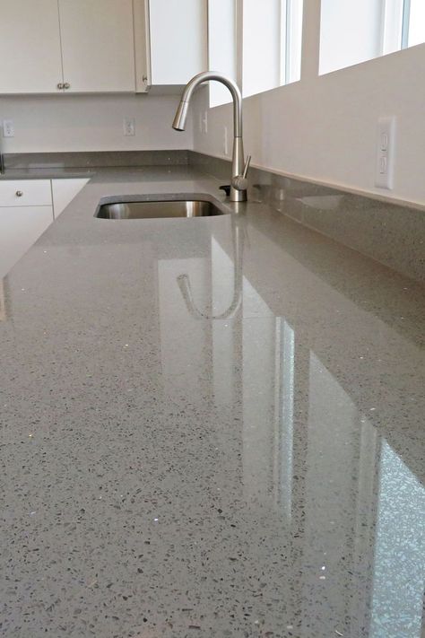 Close up of a countertop that is gray with black and silver flecks in it. Undermount sink with arched faucet and white cabinets with silver pulls are in the background Quartz Kitchen Countertops Sparkle White Cabinets, Sparkle White Quartz Countertop With Backsplash, White Quartz Countertop Sparkle, Sparkly White Countertops, Sparkly Quartz Countertops, Kitchen Sinks With White Countertops, Non White Kitchen Countertops, Kitchen Design Quartz Countertops, Quartz With Sparkle Countertops