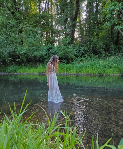 A girl in a white dress stands in the middle of the river by a forest. It appears she is floating White Dress River Photoshoot, White Dress Forest, White Dress In Water, Creepy Cottagecore, River Photoshoot Ideas, Scarlett Aesthetic, River Shoot, River Photoshoot, Goddess Photography