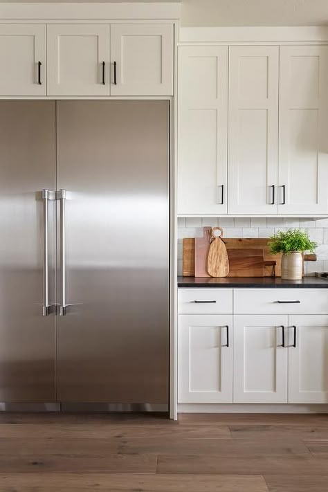 A stainless steel double door refrigerator is recessed beneath white shaker cabinets finished with oil rubbed bronze hardware. Kitchen Hardware White Cabinets, Stainless Fridge, Steel Double Doors, White Shaker Kitchen Cabinets, Stained Kitchen Cabinets, Kitchen Styling Modern, Stainless Steel Kitchen Appliances, Large Fridge, Stainless Steel Fridge