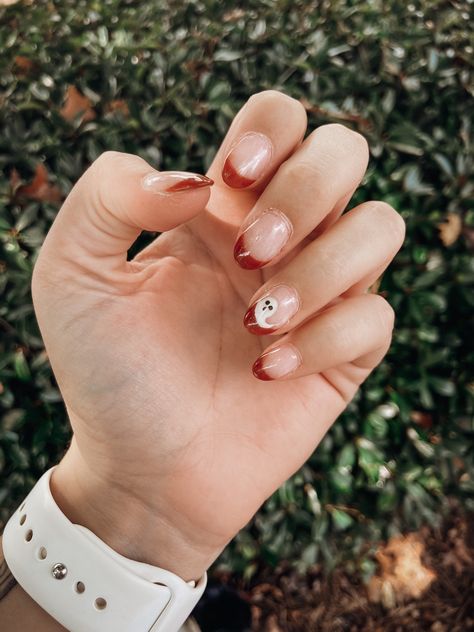 Hand with french manicure with a burnt orange color. One small ghost drawn on the ring finger. Ghost Oval Nails, Fall Time Nails Simple, Fall Nail Designs Ghost, Dip Nails For Halloween, Fall Themed Short Nails, Fall French Dip Nails, Ghost Dip Nails, Neutral Ghost Nails, Rounded Fall Nails