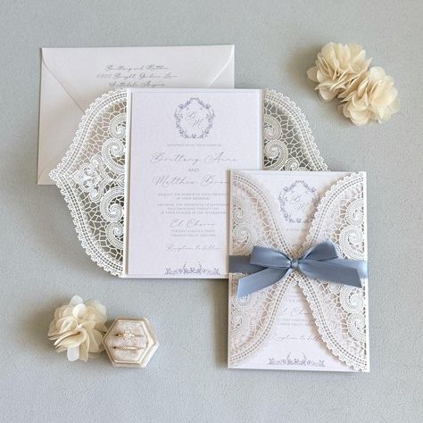 This elegant dusty blue wedding invitation features a vintage custom design, complete with lace and a handmade touch. Personalize your celebration with a botanical monogram crest on this exquisite custom wedding card, perfect for your special day. Invitations printed on White metallic card stock and mounted to the inside White laser cut folder with Dusty Blue ribbon.  Envelopes in White metallic.  I N C L U D E S - 5" X 7.25" Lace Laser Cut Folder with Satin bow - Printed Invitation mounted to t Nantucket Beach Wedding, 2025 Wedding Invitations, White Blue And Gold Wedding, Dusty Blue And Champagne Wedding, Cornflower Blue Wedding Invitations, Blue Invitations Wedding, Diy Wedding Invitations Handmade, Vintage Glam Wedding Invitations, Blue And White Wedding Invitations