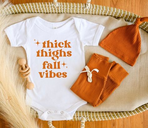 Thick Thighs Fall Vibes Onesie®. Super cute and trendy Thanksgiving outfit for newborns, infants, and toddlers. Buttery-soft cotton. Unisex design can be dressed up or down. Perfect for fall, pumpkin patch, and Thanksgiving pictures.  Onesie® sizes are available in: newborn, 3-6m, 6-9m, 12m, 18m, 24m T-shirt sizes are available in: 12m, 18m, 2T, 3T, 4T Larger sizes may be available upon request Colors available:  White with black text  Natural with black text  Black with white text White with or Fall Onesies, Onesie Designs, November Baby Shower, Fam Goals, Fall Onesie, Baby Thanksgiving, Toddler Thanksgiving, Thanksgiving Toddler, Thanksgiving Onesie