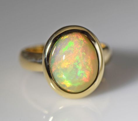 "A fiery Ethiopian Welo opal with large flashes of orange, yellow, and and green fire is bezel set in a 14k yellow gold ring. Opal is a birthstone for October and the 14th wedding anniversary gemstone. The natural opal is from Ethiopia and measures 12.5 x 10 mm oval and weighs 3.53 carats, cut in our shop The metal is 14k yellow gold  The ring is 15.5 mm wide at the stone, the shank is 4 mm wide, and the height is 8 mm  Ring weight 7.21 grams Size 6 1/2  In 2008, a new opal deposit was found app 14th Wedding Anniversary, Stowe Vt, 21 Grams, Abstract Art Diy, Green Fire, Solitaire Rings, Ring Opal, Opal Ring Gold, Wax Casting