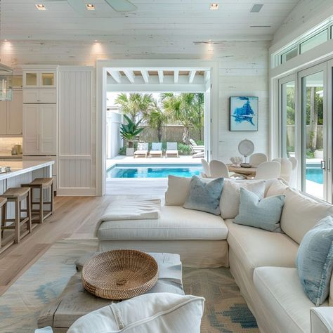 Step into this open-concept beach house, where white oak flooring and shiplap walls painted a brilliant off-white create a serene backdrop. Light blue and cream accents evoke coastal charm in the living room, featuring a plush sofa with views through large windows to the backyard pool. The space blends modern farmhouse style with beach decor, illuminated by natural light, perfect for a relaxed pool house vibe. Old House Living Room, Blue Coastal Living Room, Beach House With Pool, Cozy Beach House, Living Pool, Coastal Decorating Living Room, White Oak Floors, Coastal Living Room, Barbie House