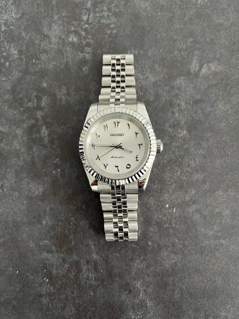 This watch is based on the Datejust with Arabic numerals. Rolex was one of the first luxury watch brands to produce watches with Arabic numerals back in the 1950s. They continued producing these for the Middle Eastern markets until the late 1970s. It wasn't until 2016 that Rolex reintroduced the dials with Arabic numerals. First for the Day Date, which was shortly after followed by the Datejust and the Daytona. In recent years the dials with Arabic numerals have become quite popular. Various brands (e.g., Breitling, Patek Philippe, Audemars Piguet, Jaeger LeCoultre, IWC) have started producing dials with Arabic numerals. Watches with Arabic numerals have been featured on the wrists of Cristiano Ronaldo, Jay-Z, Drake, DJ Khaled, Tom Brady and Mark Wahlberg.The white/silver sunburst dial wil Watch Rolex Men's, Arabic Dial Watches, Rolex Arabic Dial, Seiko Datejust, Designer Jackets For Men, Seiko Mod, Rolex Watches For Men, Luxury Watch Brands, Dj Khaled