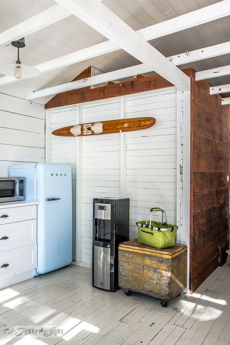 A blue smeg fridge, water ski wall art, painted floors and planked vaulted ceilings in a dreamy white shiplapped lake cottage at Cultus Lake, BC White Lake House Interiors, Small Lake House Renovation, Eclectic Lake House, Antique Lake House, Cozy Kitchenette, Small Beach Cottages Interior, Lake Bulkhead Ideas, Lake House Bunk Rooms Cottage, Retro Lake House Aesthetic