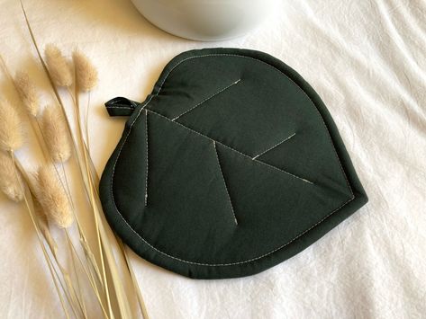 "A sweet potholder shaped like a leaf, and quilted to look like leaf veins.  The outer fabric is a dark emerald green cotton and the inner layers are Insul-bright, which is heat resistant up to 400 degrees Fahrenheit, and a layer of cotton batting.   🌿Potholder is NOT microwaveable🌿 ✨Find the matching coaster set in my shop!  This would make a beautiful addition to any \"outside-in\" kitchen, and is wrapped, ready to gift, in all eco friendly packaging!  🌻 The dimensions are approximately 8x8