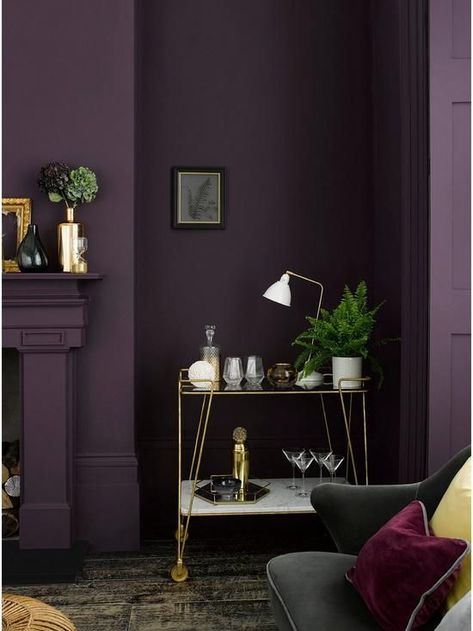 a moody living room with an aubergine accent wall, a fireplace, a delicate gold bar cart and a black sofa with colorful pillows Deep Purple Wall Color, Deep Purple Room Ideas, Deep Purple Walls, Dark Purple Wall Paint, Purple Walls Living Room, Dark Purple Living Room, Dark Purple Room, Plum Living Room, Dark Purple Wall