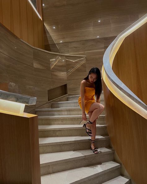 Young woman wear orange summer dress styled with black strappy block heels standing in a staircase in hotel lobby Poses In Heels And Dress, Poses On Stairs Instagram Dress, Tying Shoes Pose, Photo Ideas Stairs, Poses With Heels, Pictures On The Stairs, Orange Heels Outfit, Staircase Poses, Stairs Poses