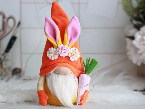 "A gnome rabbit with pink carrots and flowers is a great addition to the decor of the home for spring and Easter. This bright gnome will give you a smile and a good mood for the whole day. DETAILS: - The body is made of fleece.Holofiber was use as a filler. - The hat is made of orange fleece and decorated with flowers. - The beard is made of faux fur. - The carrot is made of fabric. SIZE GNOME: Height 11\" (28 cm), diameter of base 3\" (8 cm). You can see other easter gnomes in my store at the l Easter Dolls, Playful Expression, Doll Decoration, Easter Plush, Easter Decorating, Easter Gnome, Gnome Gift, Bunny Figurine, Rabbit Dolls