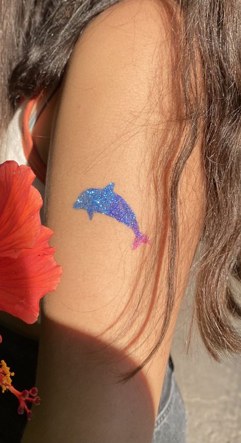 girls arm with a dolphin glitter tattoo on it. the tattoo is blue pink and purple Glitter Tattoo Summer, Glitter Tattoo Aesthetic, Coconut Girl Tattoo, Glitter Tattoo Ideas, Beach Girlies, Bestie Crafts, Coconut Tattoo, Glitter Henna, Sparkle Tattoo