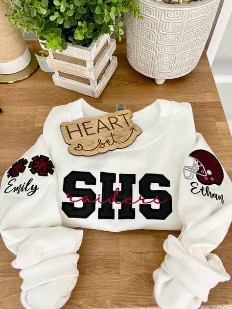 ** Please read before buying **  Personalized Embroidered School Spirit sweatshirt with glitter HTV applique. Fit: Unisex, Fits loose/relaxed Sizing: S,M,L,XL,2XL Material: 50% Cotton, 50% Polyester Embroidery Details: School initials with mascot name centered across the chest Pom pom's with personalized name on right shoulder sleeve Helmet with personalized name on left shoulder sleeve *If you don't see what you're looking for please message me. :)  PROCESSING/TURNAROUND TIME: -Processing/Turn Multi Sport Mom Shirt, Football School Shirts, Cheer Mom Sweatshirt Ideas, School Sweatshirts Designs, Cheer Camp Outfits, Cheer Sweatshirts, Cheer Jackets, Football Merch, Sports Embroidery