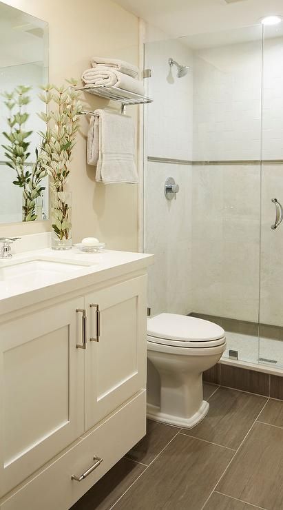 Small welcoming cream bathroom features a cream washstand placed on wood like floor tiles and fitted with a bottom drawer, satin nickel pulls, and a white quartz countertop holding a sink with a polished nickel faucet beneath a framless vanity mirror mounted to a cream wall. Cream Bathroom, Trendy Bathroom Tiles, Narrow Bathroom, Budget Bathroom Remodel, Bathroom Tub, Diy Bathroom Remodel, Bathroom Remodel Shower, Trendy Bathroom, Budget Bathroom