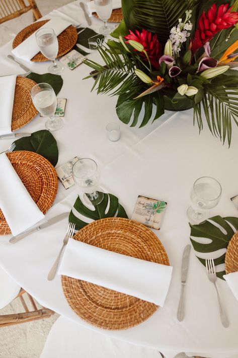 Elegant tropical reception decorations for your beach wedding. The reception table is decorated with a rattan charger, white table cloth, a white napkin, a monstera leaf and a tropical centerpiece. Save for inspiration. Boho Tropical Wedding Table Decor, Tropical Centerpieces Wedding Receptions, Tropical Garden Wedding Decor, Tropical Place Cards, Minimal Tropical Centerpiece, Monstera Leaf Table Decor, Beach Wedding Reception Table Decor, Beach Wedding Reception Ideas Table Decorations, Wedding Table Tropical