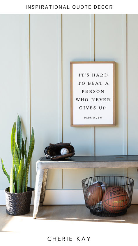 Framed wall sign with an inspirational quote by Babe Ruth, "It's hard to beat a person who never gives up," displayed on a light green paneled wall above a metal bench. The scene includes a baseball glove with a ball, a potted snake plant, and a black wire basket with sports balls, creating a sporty and motivational decor perfect for kids' rooms, sports-themed spaces, or office decor. Babe Ruth Quotes, Sports Office, Sports Decor, Quote Decor, Kids Room Wall Decor, Babe Ruth, Sports Decorations, Themed Decor, Office Spaces