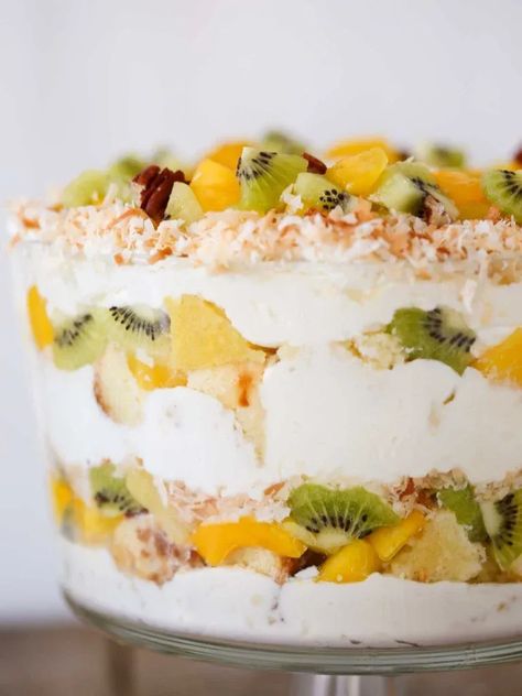 This Tropical Trifle recipe is easy, delicious and showstopping! Layers of rum soaked cake, coconut cream, mangoes, kiwi and pineapple! Add some of the reserved fruit, coconut and pecans around the edge for a showstopping presentation! Tropical Fruit Desserts, Tropical Trifle Desserts, Hawaiian Trifle, Pina Colada Trifle, Fruit Trifle Desserts, Tropical Trifle, Coconut Trifle, Tropical Food Recipes, Orange Trifle