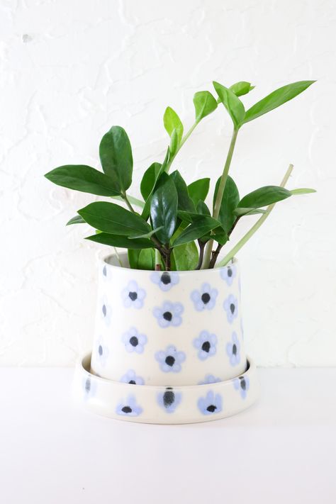 Dress up your houseplant in these handmade planters. Opening is ideal for a 4” nursery pot. Each plant home features a drainage hole, and matching saucer. Lovingly handmade in Portland, Oregon. Perwinkle flowers adorn a white clay body. Ceramic Pot Design, Ceramic Pot Design Ideas, Flower Painted Pottery, Ceramic Diy Ideas, Plant Ceramics, Ceramic Design Ideas, Plant Pot Designs, Nursery Pottery, Plant Pot Painting