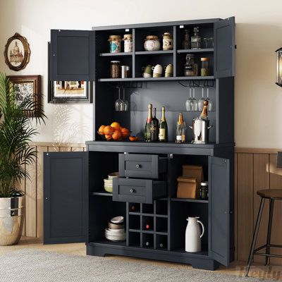 This freestanding bar cabinet gives you a convenient spot to brew coffee and concoct cocktails. The upper section features two open shelves and two cabinets with doors, while below are two drawers and even more storage space for plates, mugs, and barware. Nine cubbies also give you a place to store your favorite bottles of wine. The main prep area comes with hanging racks for stemware and ample room for a coffee maker and mixology essentials. It features a unique exterior design with classic col Bar Cabinet Kitchen, Coffee Bar Cabinet, Kitchen Cupboard Storage, Farmhouse Coffee Bar, Pantry Storage Cabinet, Kitchen Buffet, Kitchen Pantry Storage, Kitchen Glass, Wine Cabinet