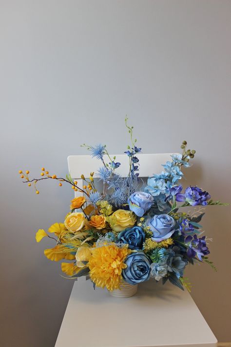 Adorn your table with the radiant charm of our blue and yellow centerpiece, a splendid addition perfect for weddings or a delightful springtime affair. This silk flower arrangement, carefully crafted to capture the essence of the season, exudes a vibrant and refreshing aura. With a harmonious blend of blue and yellow hues, this centerpiece illuminates any setting, bringing forth a cheerful and inviting atmosphere. Its captivating design not only serves as a focal point but also infuses the space Blue Yellow Decorations Party, Blue Arrangements Flower, Blue Flower Arrangements Table, Blue And Yellow Flower Arrangements, Blue And Yellow Wedding Flowers, Blue Flower Centerpieces, Yellow Floral Decor, Yellow And Blue Wedding, Yellow Centerpiece