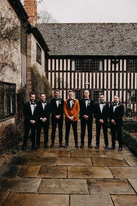 Groomsmen wearing classic black grooms suits with bowties standing with groom in crushed burnt orange velvet grooms blazer, black bowtie and black suit trousers outside Brinsop Court wedding venue | Jessica Grace Photography Burnt Orange Bridesmaid Dresses With Groomsmen, Black Wedding Dress Orange Bridesmaids, Black Orange Wedding Theme, Rust Orange And Black Wedding, Burnt Orange And Black Wedding Theme, Burnt Orange Tuxedo Wedding, Black And Orange Fall Wedding, Black And Orange Wedding Theme, Burnt Orange Groomsmen Attire