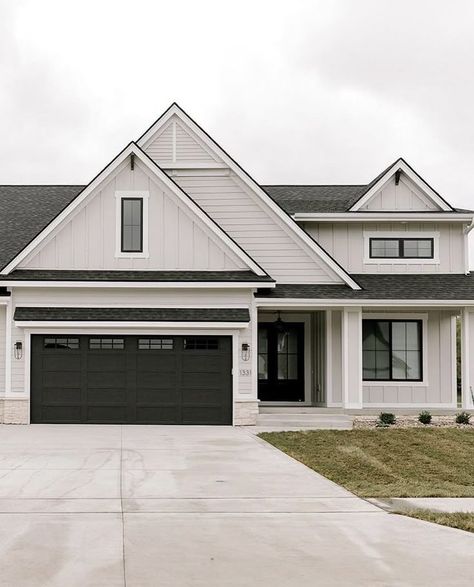 Grey House White Garage Doors, Light Grey Vertical Siding, Ivory And Black House Exterior, White Garage Exterior, Cream House Dark Trim Exterior, Tan Black House Exterior, White House Dark Grey Roof, Taupe House Exterior Black Trim, Grey Exterior Farmhouse